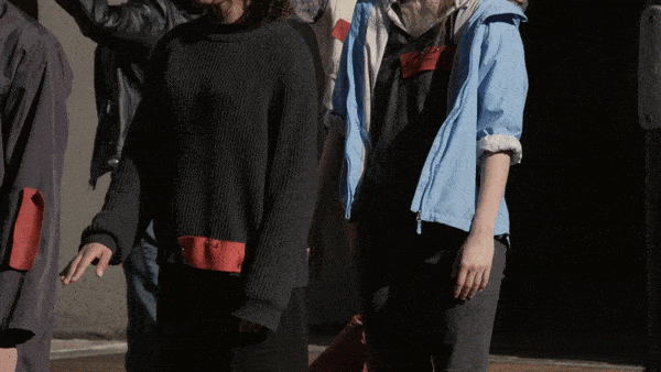 Close-up gif of two peoples’ hands slowly deconstructing a fictional salute in the midst of a clapping crowd